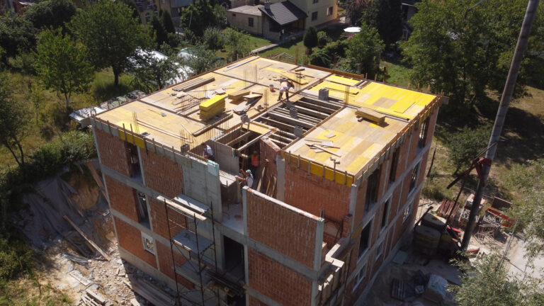 Stambeni objekat u fazi izgradnje, s vidljivom konstrukcijom, radnicima i građevinskim materijalom na gradilištu